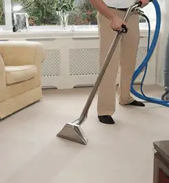 Professional carpet cleaner using a hot-water extraction wand and hose machine in a living room in Stockton, CA.