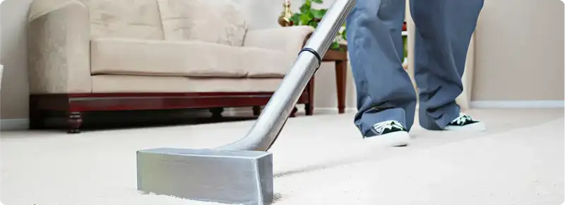 Carpet cleaning technician using a hot-water extraction wand on a light-colored carpet in a living room, Stockton, CA.