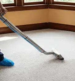 Steam carpet cleaning technician using a hot-water extraction wand on a residential carpet, wearing blue protective shoe covers Stockton, CA.