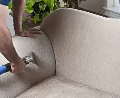 Professional upholstery cleaner deep-cleaning a fabric sofa with a handheld extraction tool and hose in Stockton, CA.